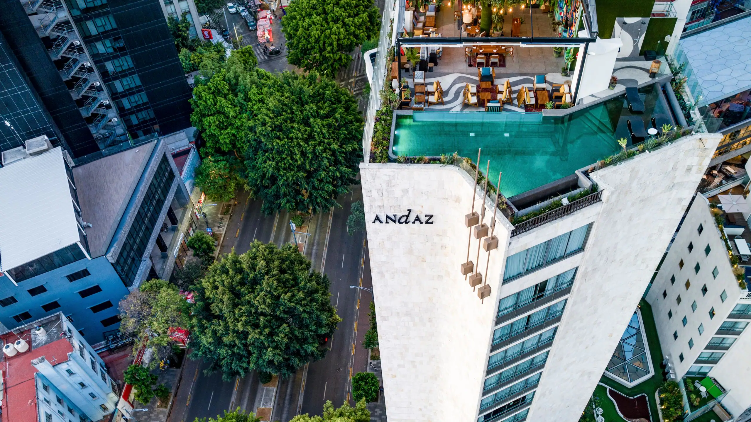 A striking aerial view of the Andaz Mexico City hotel, showcasing its rooftop pool, modern architecture, and the tree-lined streets of the vibrant Condesa neighborhood.