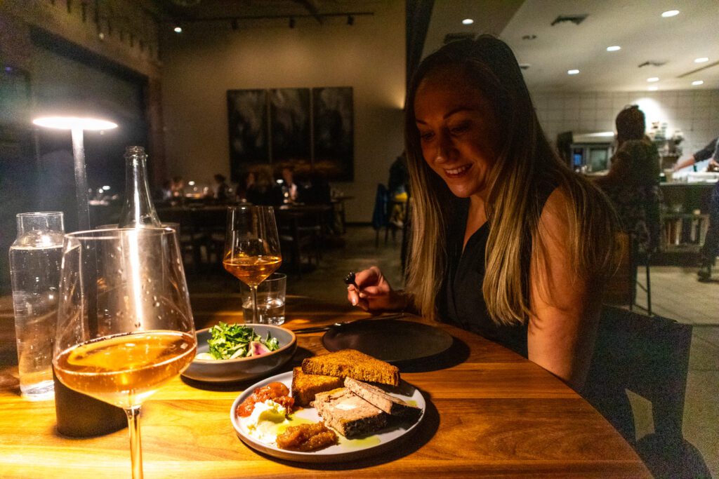 Woman smiling at a candlelit dinner table with gourmet food, salad, and glasses of wine at a modern restaurant