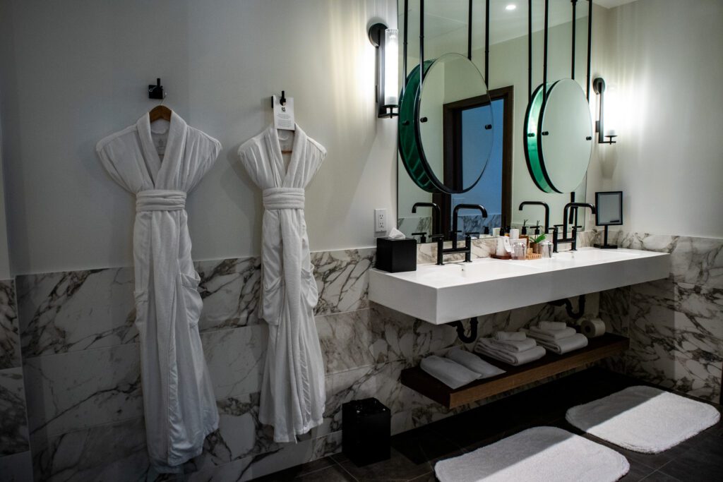 Spacious bathroom at The Estate Yountville with plush robes, marble finishes, double sinks, and circular mirrors suspended from the ceiling