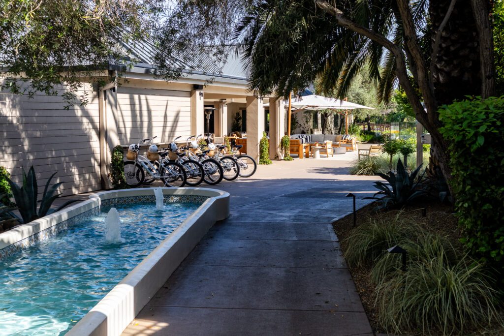 Row of cruiser bikes available for guests near a shaded outdoor seating area and water feature at The Estate Yountville.