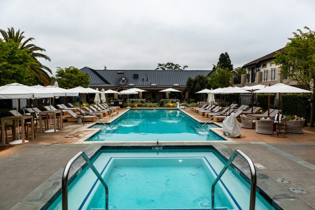 Relaxing view from the hot tub toward the pool area at The Estate Yountville, framed by palm trees and resort-style seating.