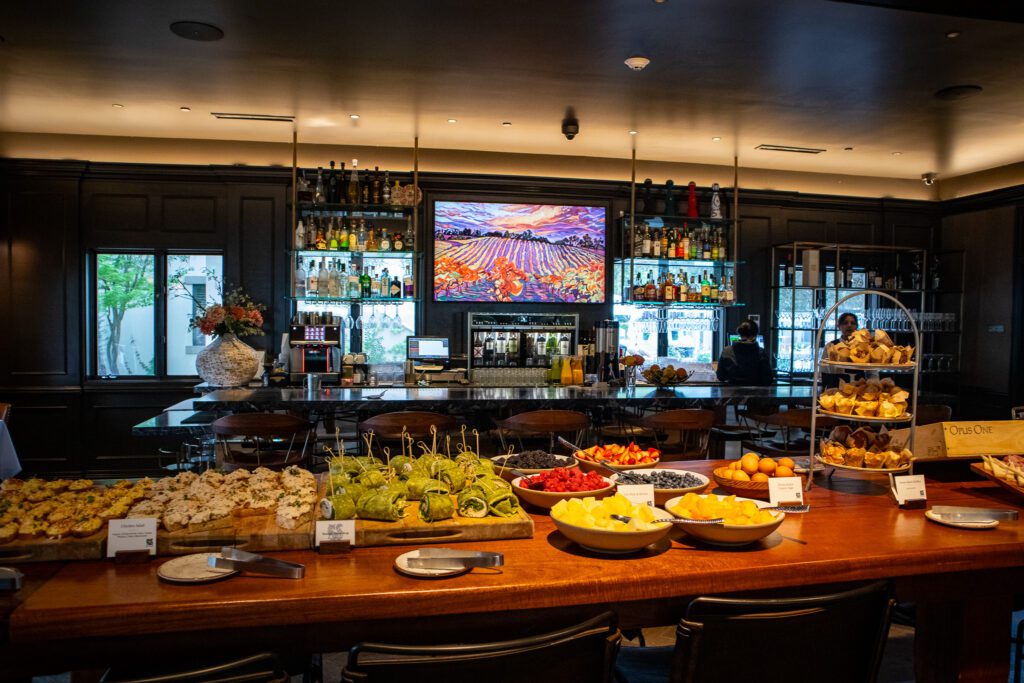 Colorful breakfast spread at The Estate Yountville featuring fresh fruit, wraps, chicken salad crostini, and a pastry tower in front of a stylish bar.