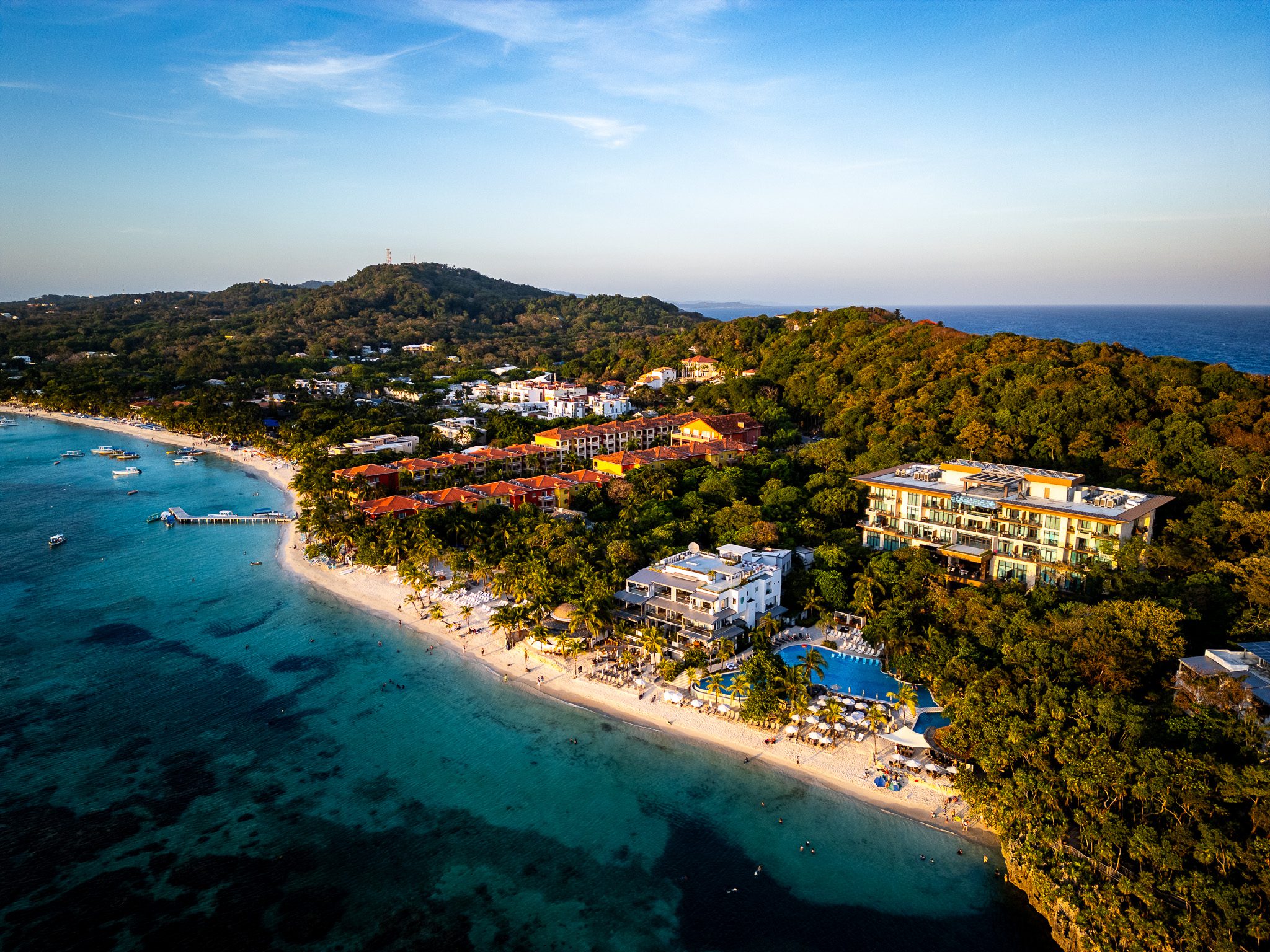 Aerial view of Kimpton Grand Roatan surrounded by lush jungle, with the resort’s pool and beachfront area in the foreground and the Caribbean Sea in the distance.