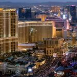Aerial night view of The Palazzo and The Venetian resorts on the Las Vegas Strip, with hotel towers lit up and the city skyline in the background.