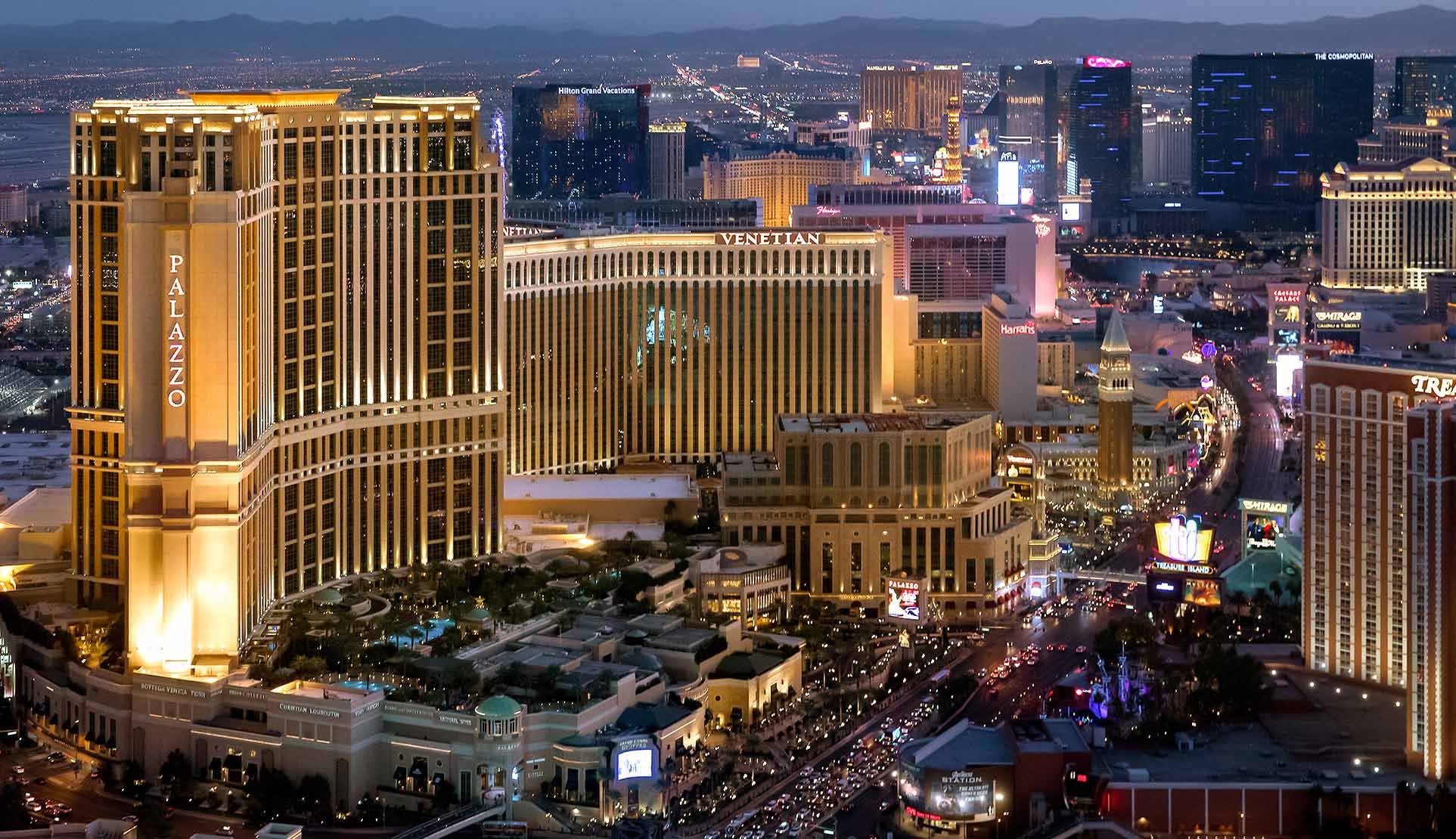 Aerial night view of The Palazzo and The Venetian resorts on the Las Vegas Strip, with hotel towers lit up and the city skyline in the background.