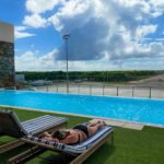 Infinity pool at the Punta Cana Airport VIP Lounge with striped loungers, modern mural wall art, and expansive runway views under bright tropical skies.