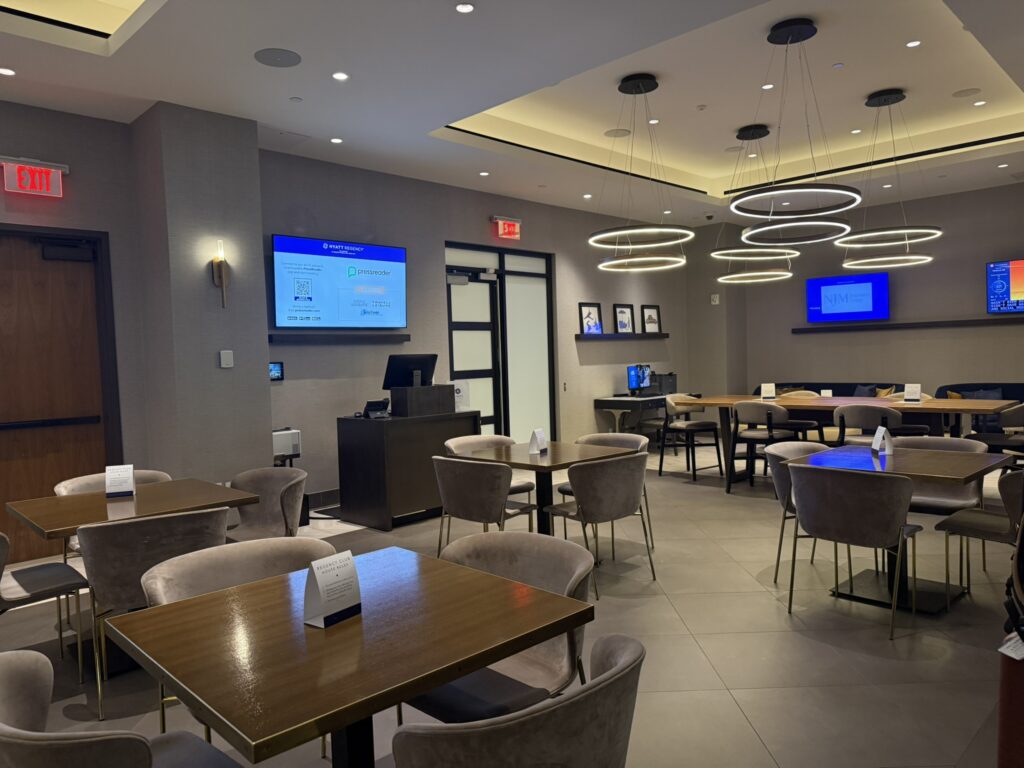 Regency Club seating area at the Hyatt Regency JFK with modern décor, dining tables, and ring pendant lighting.