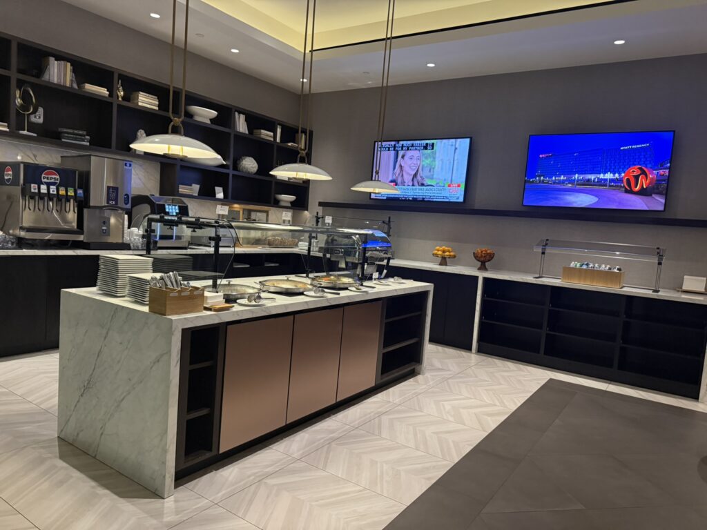 Full buffet area inside the Regency Club at Hyatt Regency JFK with counters, TVs, and self-serve drink stations.