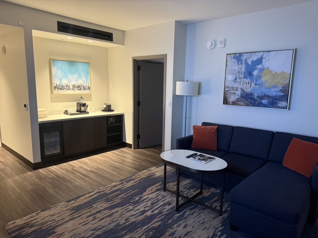 Executive Suite seating area at Hyatt Regency JFK with sectional sofa, coffee table, and kitchenette setup.
