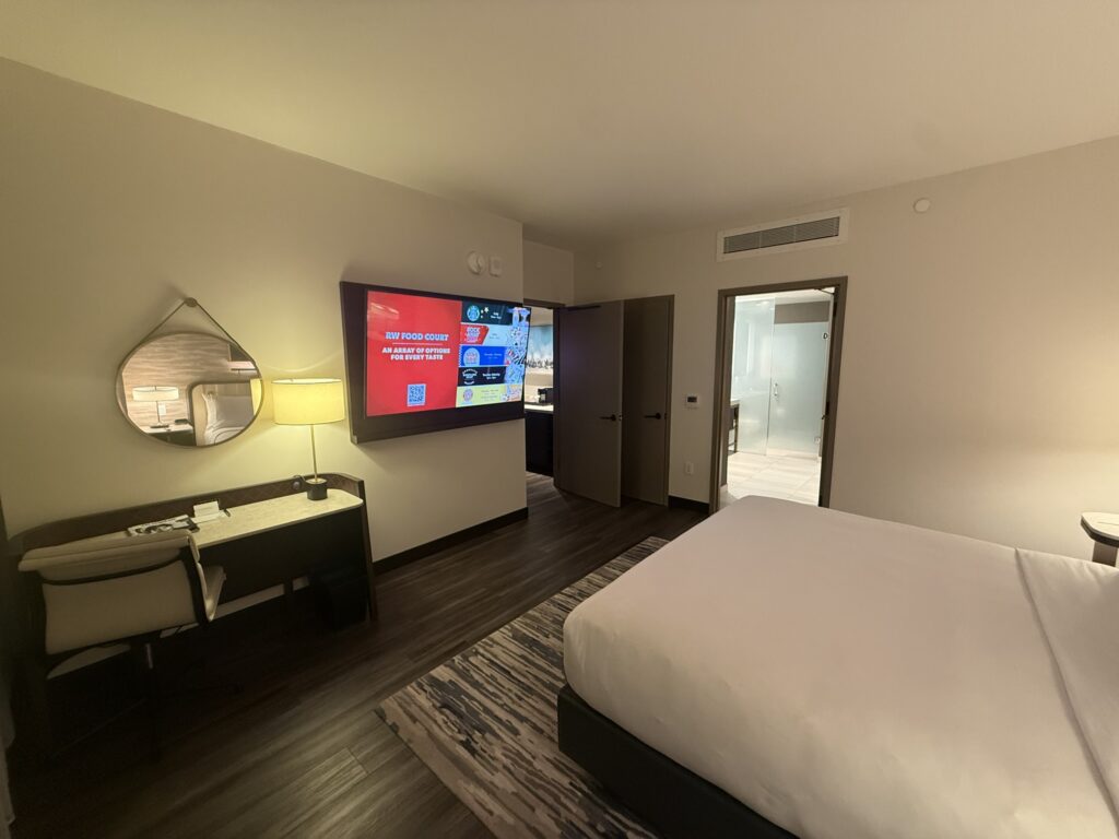 Hyatt Regency JFK bedroom with king bed, work desk, large TV, and modern decor.