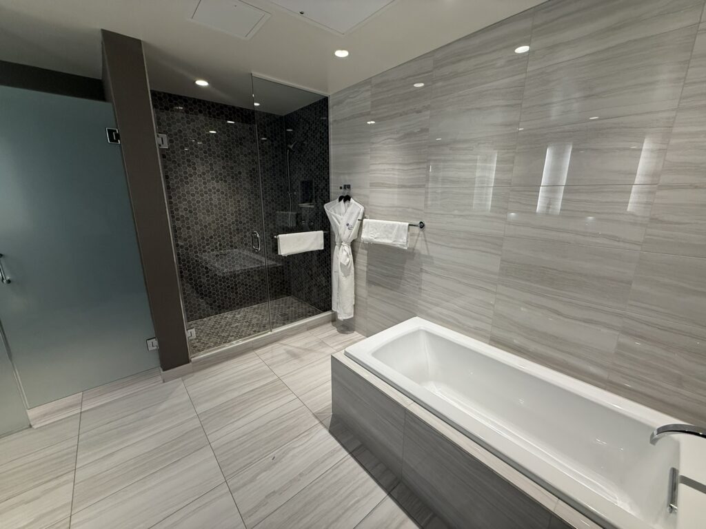 Spacious suite bathroom at Hyatt Regency JFK with a large soaking tub, glass shower, and modern tile design.