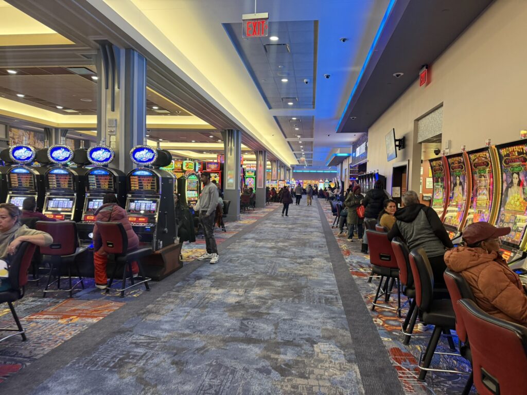 Casino floor inside Resorts World New York with rows of slot machines and guests seated throughout.