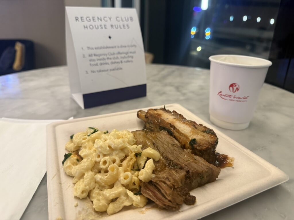 Plate of mac and cheese and braised meats in the Hyatt Regency JFK Regency Club with a “house rules” sign in the background.