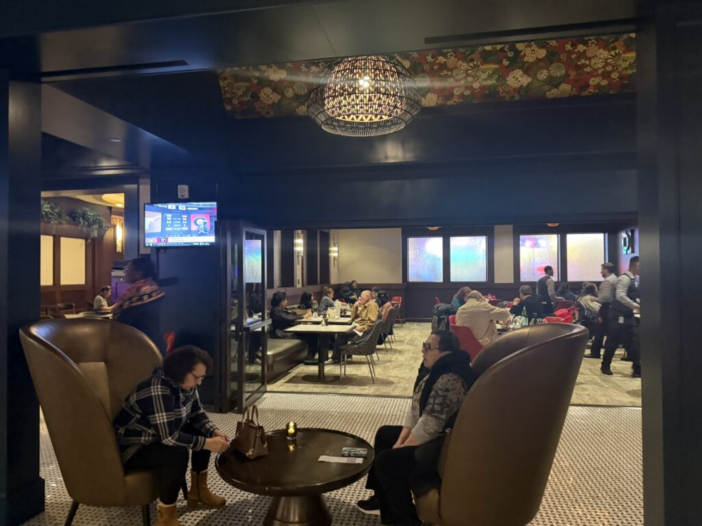 Dining room inside RW Prime at Resorts World, with guests seated in leather chairs and a TV in the background.