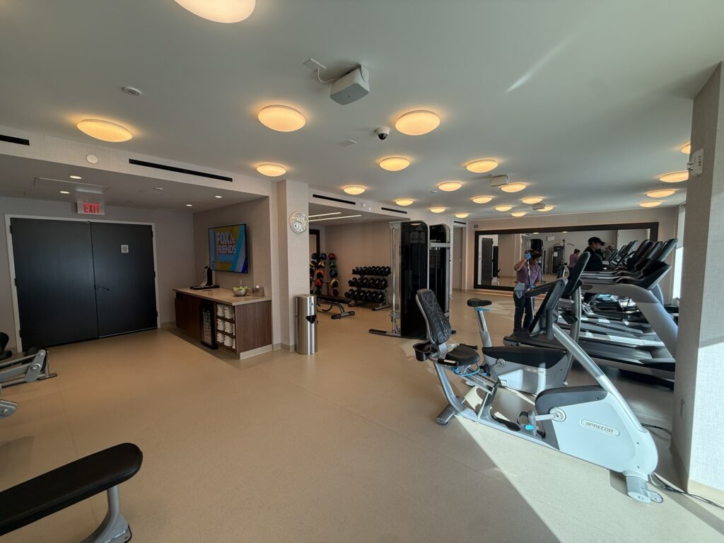 Spacious fitness center at the Hyatt Regency JFK with treadmills, weight machines, free weights, and bright overhead lighting.