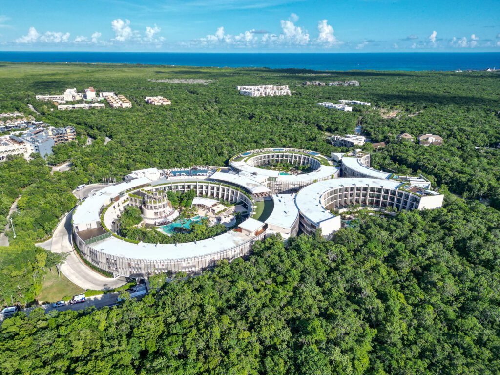 rone shot showing the circular architecture of Secrets Tulum surrounded by dense jungle with the Caribbean Sea visible on the horizon.