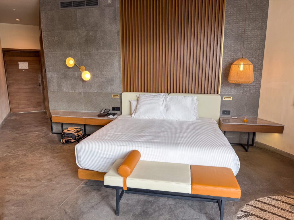 King bed with modern lighting, wood panel accents, and side tables inside a Secrets Tulum guest room.