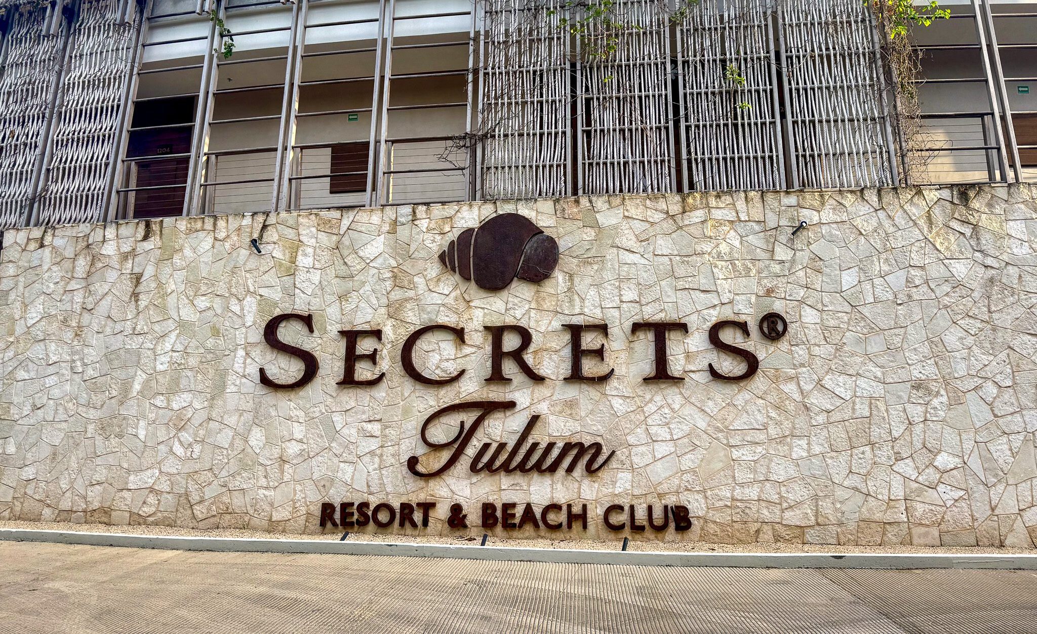 Exterior stone wall with the “Secrets Tulum Resort & Beach Club” sign and building façade above.
