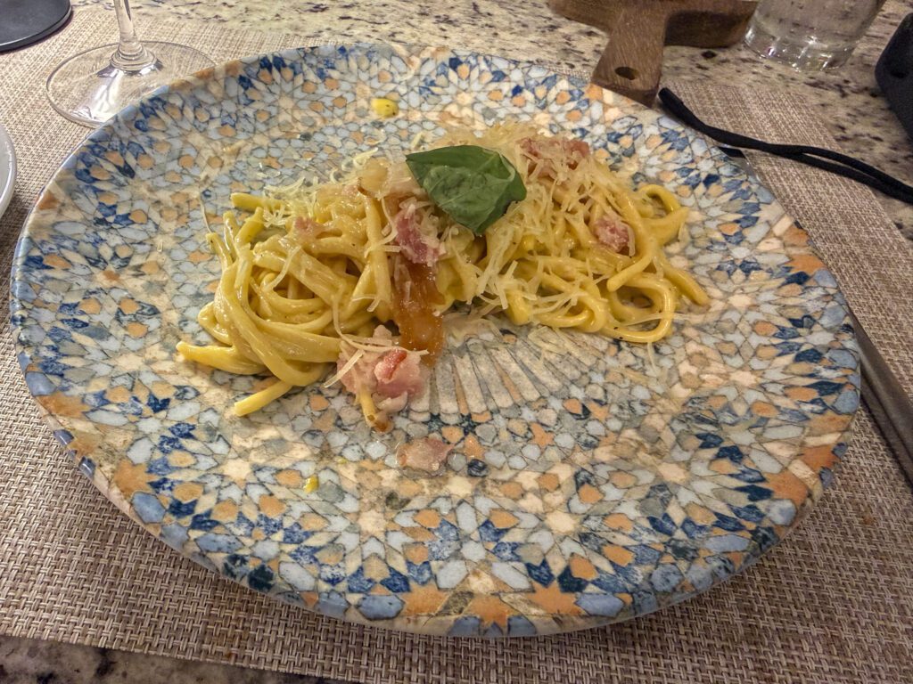 Plate of fresh pasta with cheese, tomatoes, and basil served on a decorative mosaic-style plate.