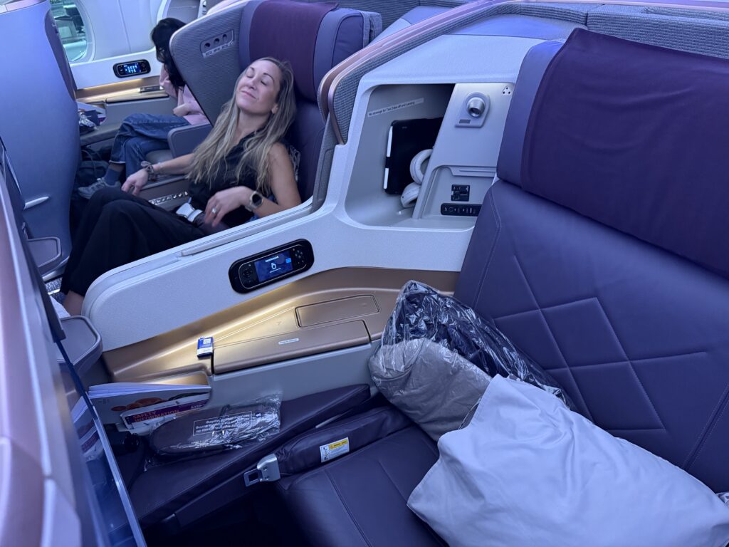 Singapore Airlines Business Class seat reclined for relaxation with wide armrests, personal storage, and mood lighting on long-haul flight.