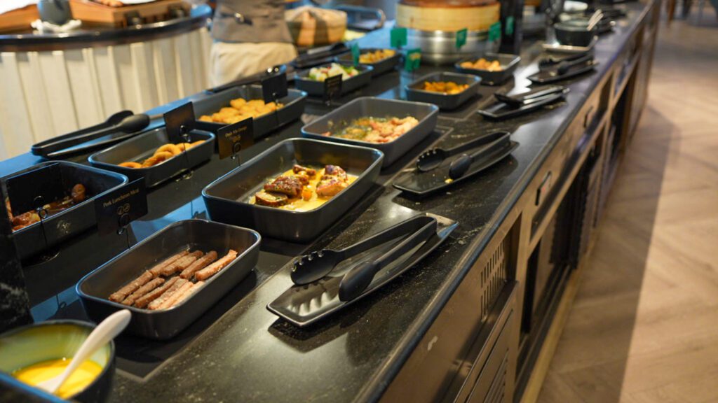 Hot breakfast buffet at the Singapore Airlines SilverKris Lounge in Changi Airport with sausages, eggs, and Asian dishes.