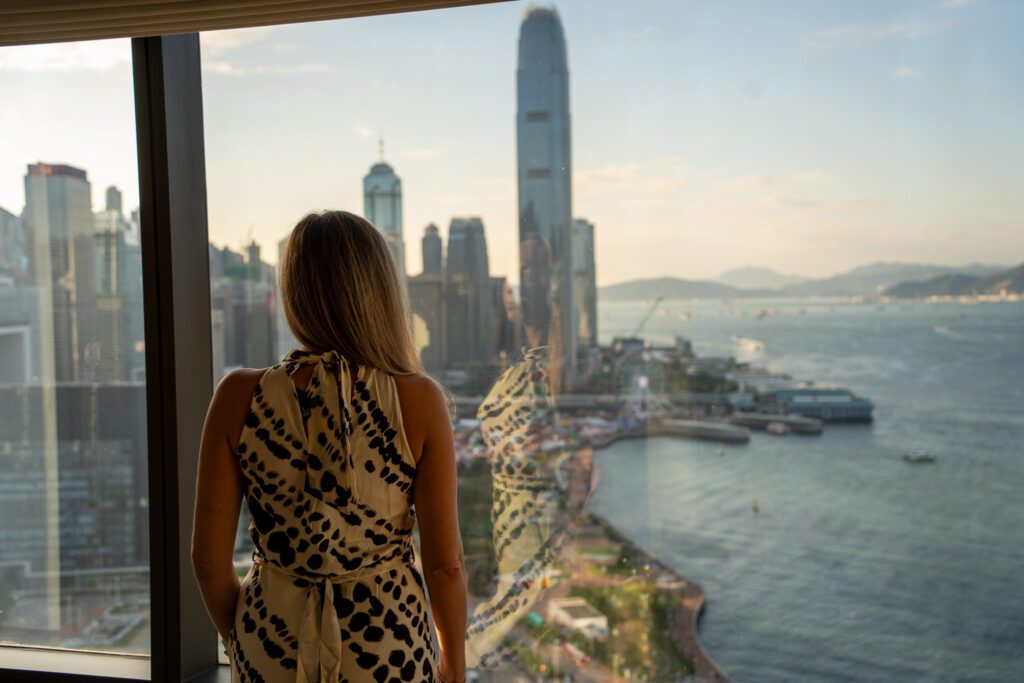 Guest standing by floor-to-ceiling windows in a Grand Hyatt Hong Kong suite overlooking Victoria Harbour and the city skyline