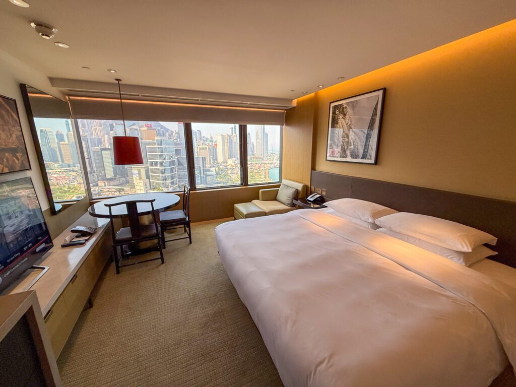 Standard guest room at the Grand Hyatt Hong Kong featuring a king bed, seating area, and floor-to-ceiling windows overlooking the Hong Kong skyline