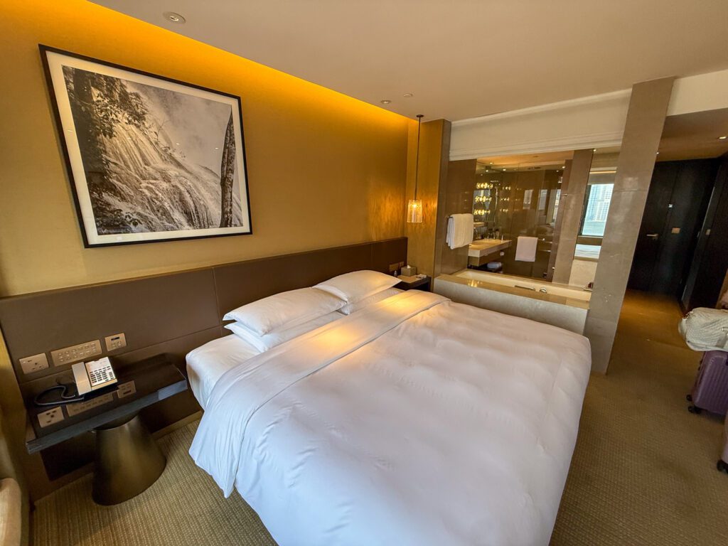 Bedroom and open bathroom layout inside a standard guest room at the Grand Hyatt Hong Kong, showing the bed, soaking tub, and modern finishes