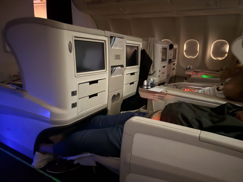 Fiji Airways A330 business class angled-flat seat fully reclined in bed mode showing limited storage compartments and footwell space.