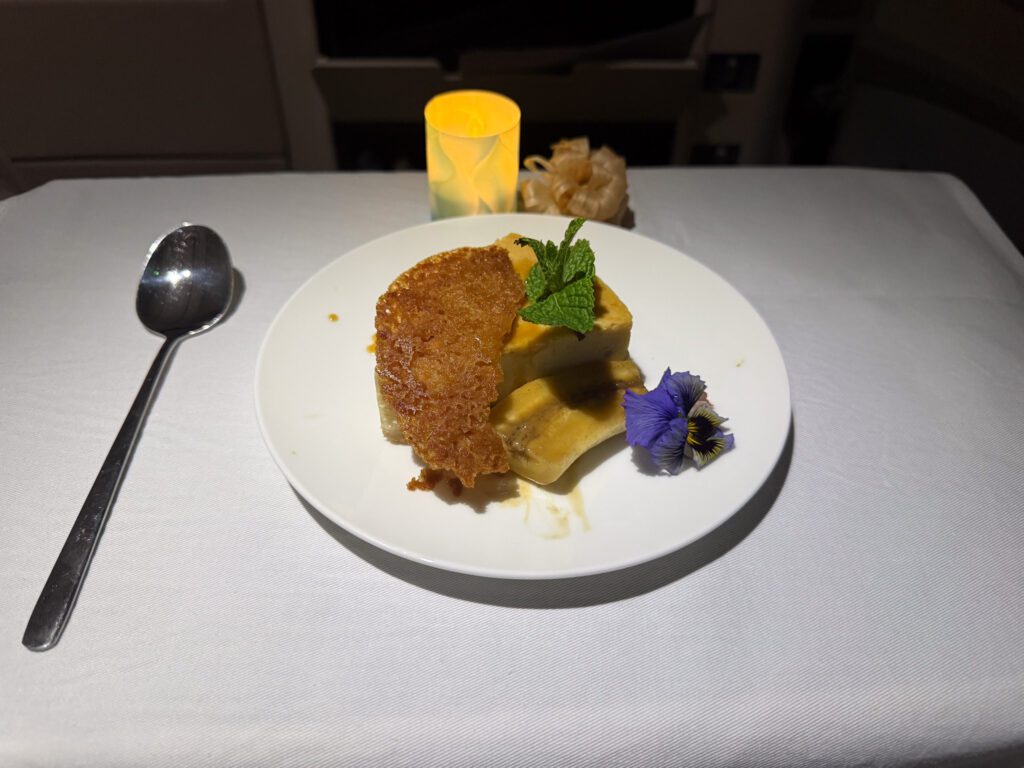 Banana macadamia cheesecake dessert served in Fiji Airways business class on the A330 from Hong Kong to Nadi, garnished with mint and edible flowers.