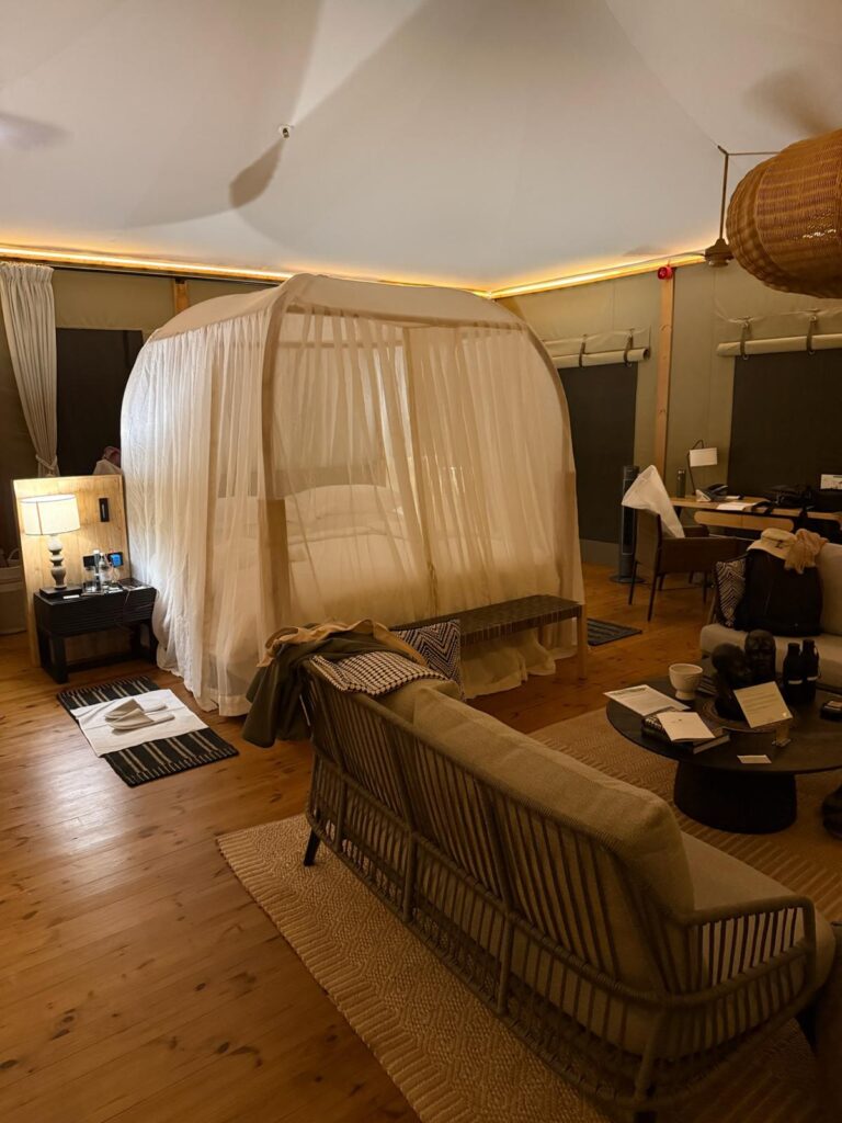 Interior of luxury tented suite at JW Marriott Masai Mara with canopy bed, lounge seating, and wood floors