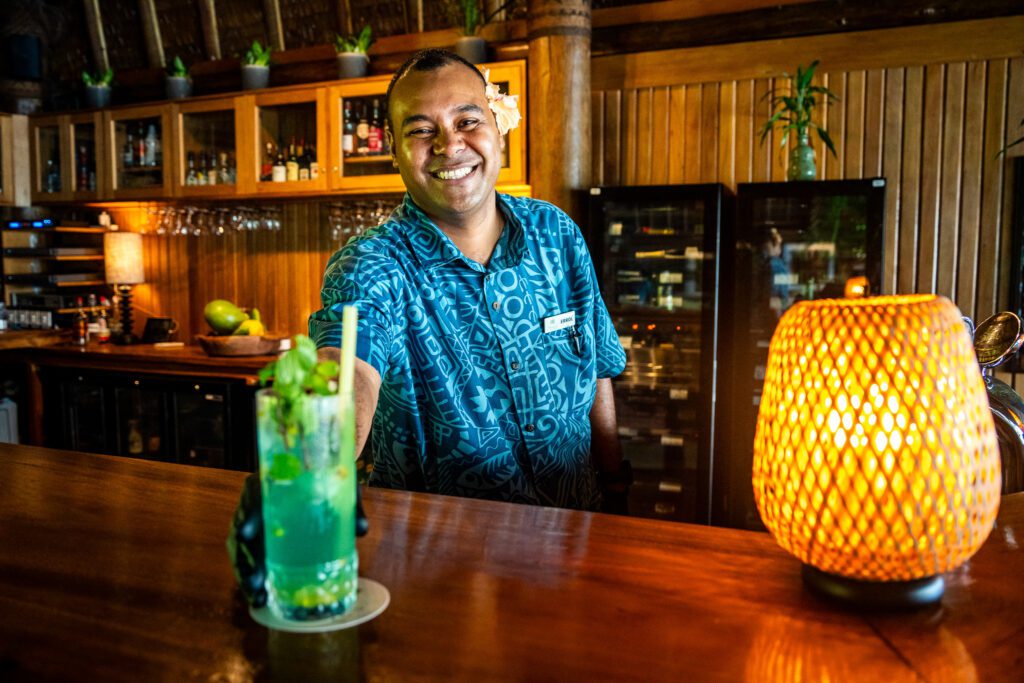 Smiling bartender serving a fresh mint cocktail at the bar inside Namale Resort & Spa in Fiji.