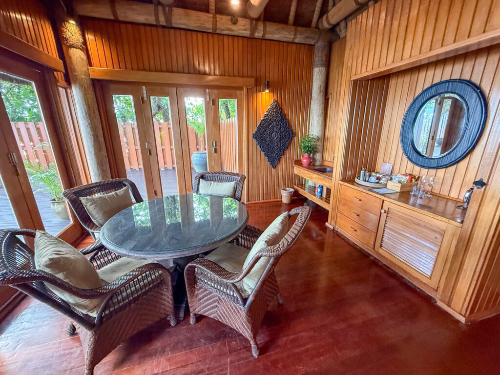 Indoor dining space with round table, wicker chairs, and stocked mini bar inside a Namale Resort villa.