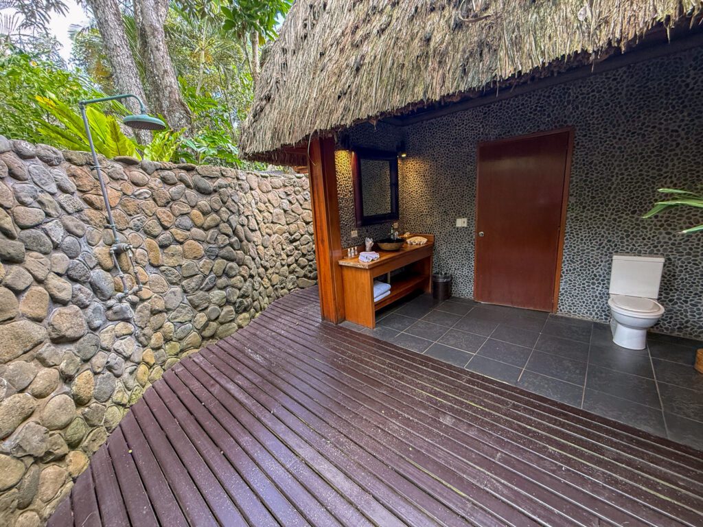 Open-air outdoor bathroom with stone wall and rainfall shower at Namale Resort in Fiji.