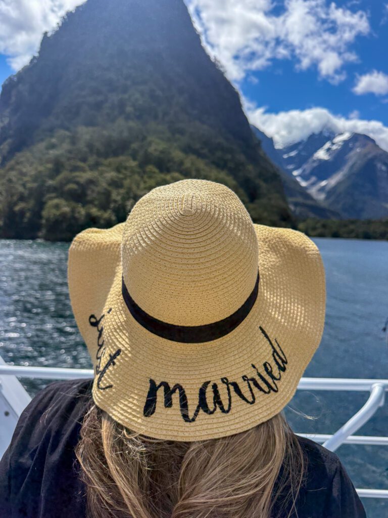 View from Milford Sound cruise boat with sun hat overlooking fjord and mountain peaks