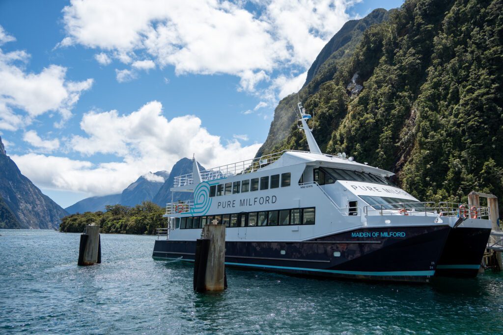 Pure Milford cruise boat docked in Milford Sound with mountains and blue sky in background