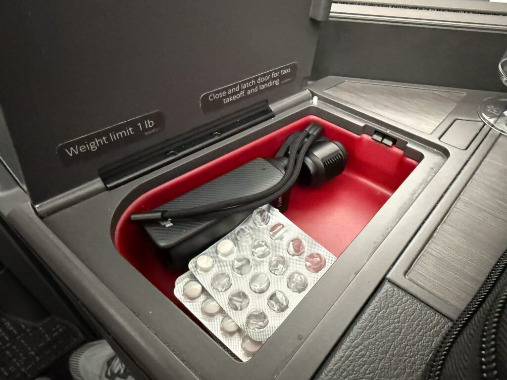 American Airlines 787-9 business class storage compartment with charging cable and personal items