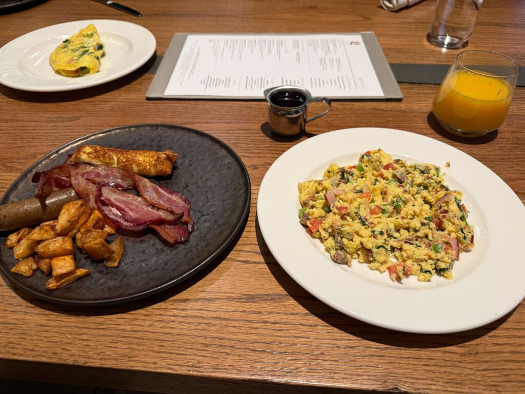 Breakfast buffet plate at Grand Hyatt Vail with scrambled eggs, bacon, sausage, potatoes, and orange juice