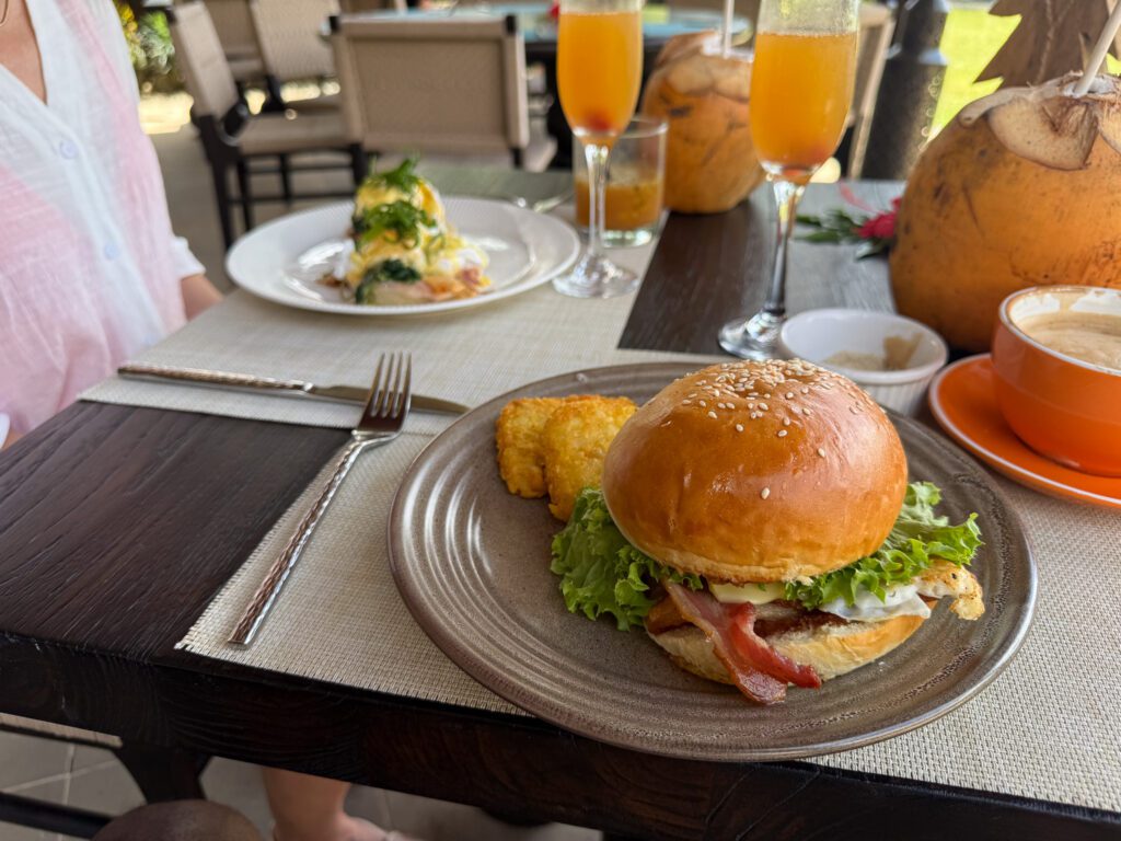 Breakfast spread at Nanuku Resort Fiji featuring tropical drinks, eggs benedict, and gourmet breakfast sandwich