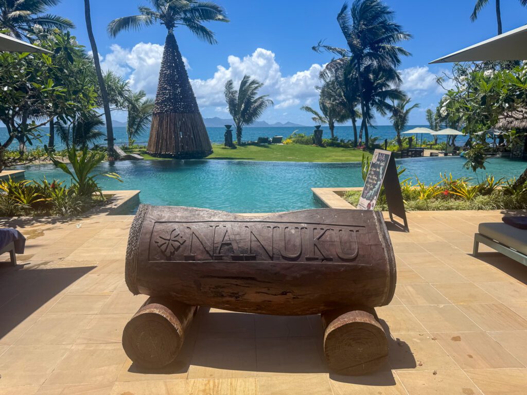 Nanuku Resort Fiji welcome sign beside the oceanfront infinity pool and palm-lined beach