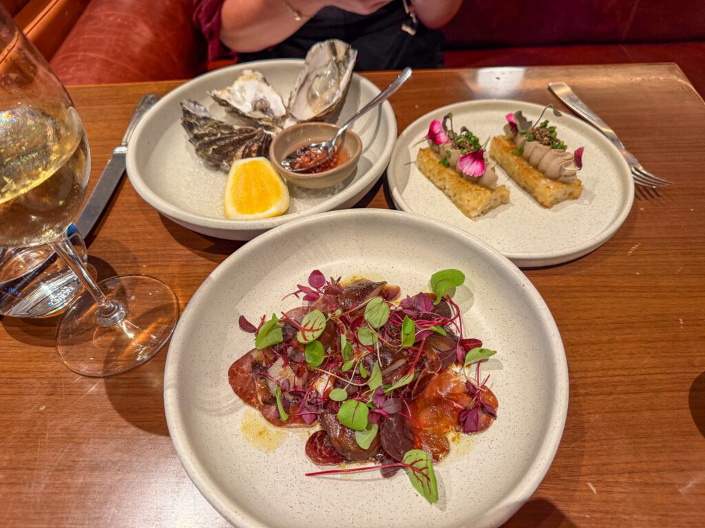 Appetizers served at Onemata restaurant at Park Hyatt Auckland featuring fresh oysters, duck liver pâté croquettes, and wagyu bresaola